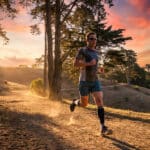 Un coureur d'âge mûr court sur un sentier en forêt au coucher du soleil.